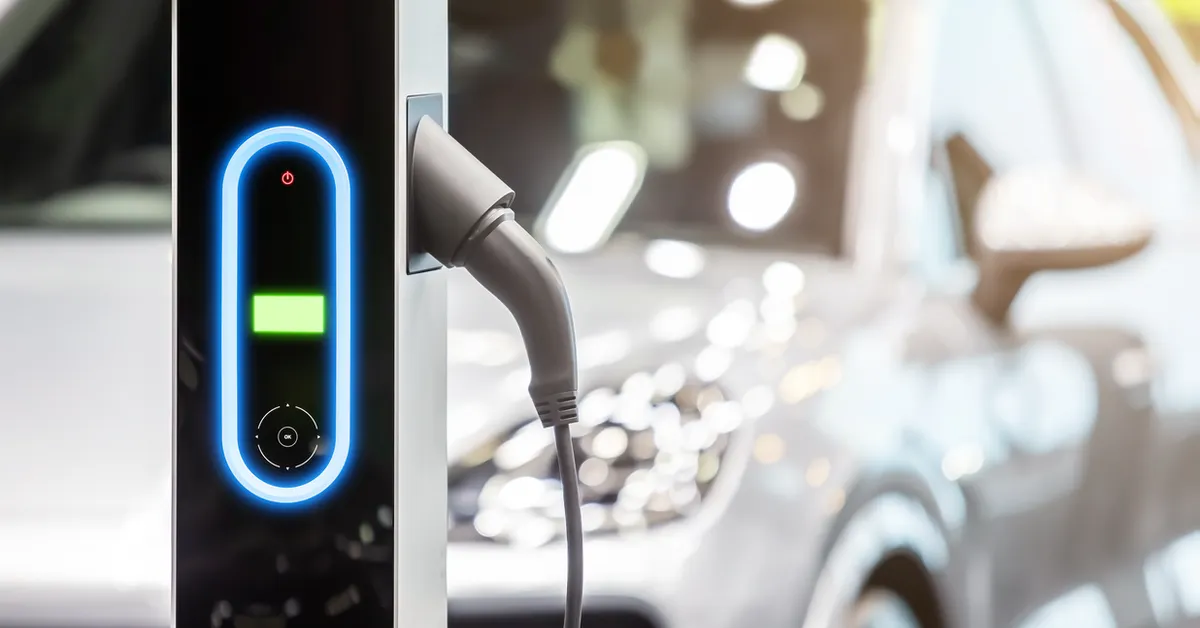 In the foreground is a public EV charger, in the background a blurred image of a car.