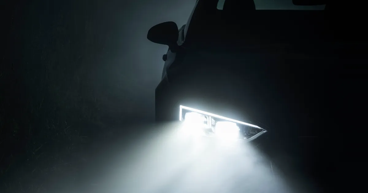 A foggy night with a car headlight visible shining through the fog.
