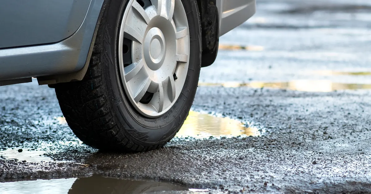 A car next to a pothole on the road.