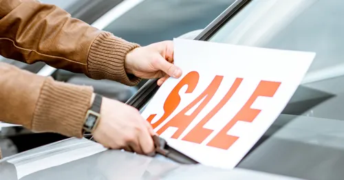 A person putting a 'sale' sign on a car windscreen.