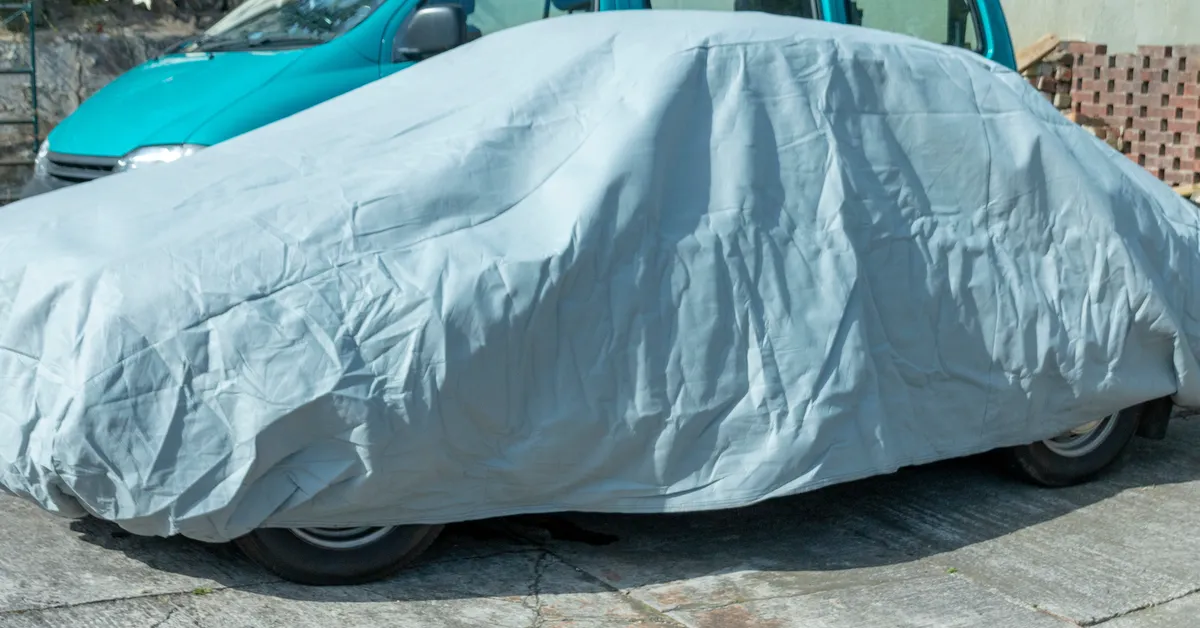 A silver car cover, with an old car underneath, on a driveway.