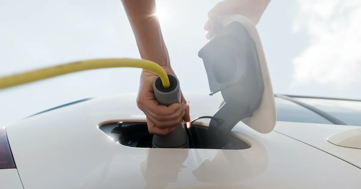 Photograph of a person plugging in an EV car charger on a sunny day.