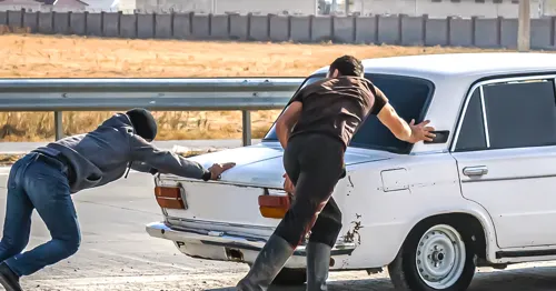 Two people pushing a car.'