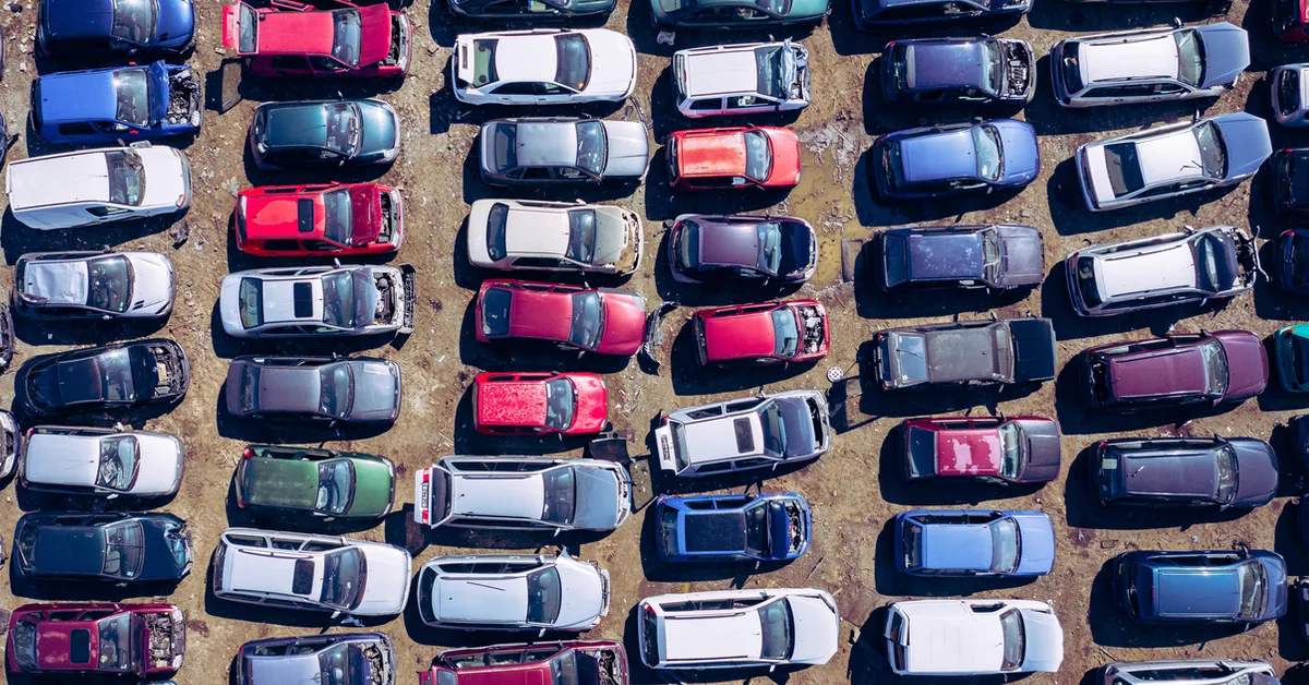A multi-coloured car scrap yard with rows of cars on a dirt surface.